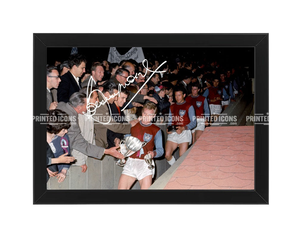 Bobby Moore signed-style photo print showing the West Ham captain carrying the FA Cup after the club’s historic 1964 Wembley victory, displayed in a black frame.